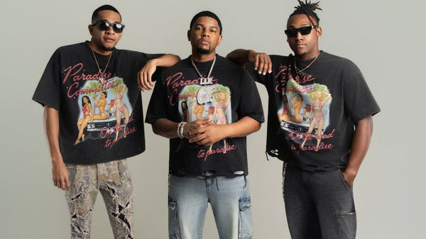Three men wearing matching graphic t-shirts standing together against a plain background